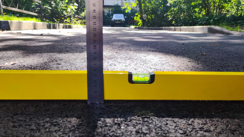 Замер просадки асфальта линейкой при проверке ровности уровнем у бордюра