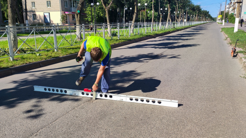 Рабочий присел у рейки и делает замер ровности асфальта рядом с ограждением