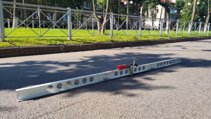 Длинная измерительная рейка лежит на дороге рядом с ограждением и зелёной полосой