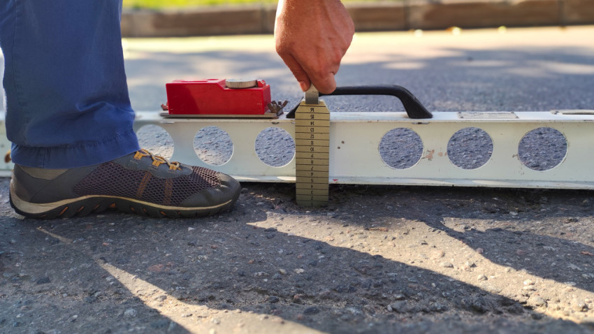 Клин-промерник и рейка на асфальте показывают глубину неровности крупным планом