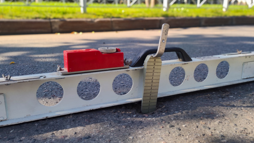 Рейка и клин-промерник на асфальте в кадре с упором на замер ровности