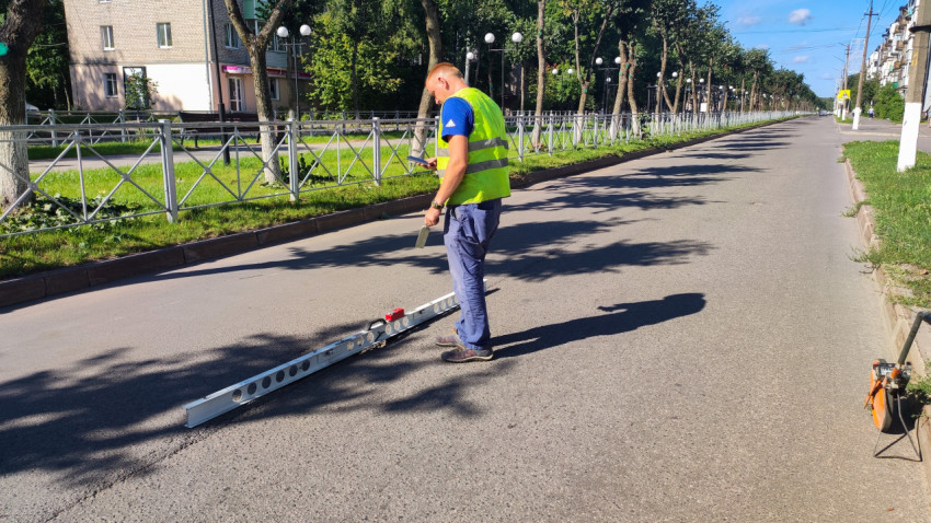 Специалист отмечает результат замера ровности на телефоне, пока рейка лежит на асфальте