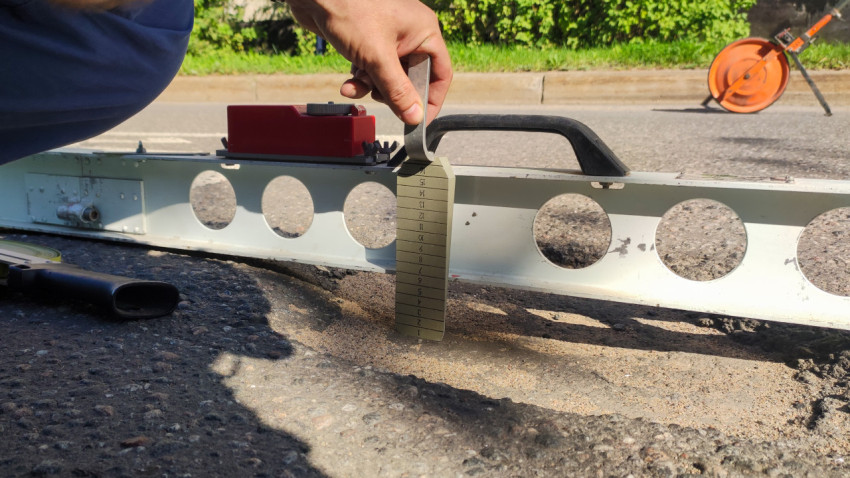 Измеряют колею на асфальте: рейка, клин-мерка и измерительное колесо на обочине