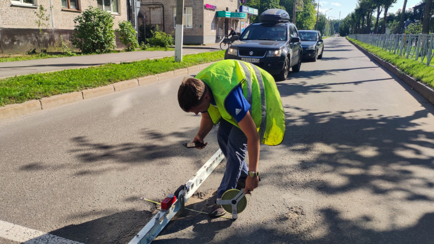 Дорожник меряет неровность на полосе, пока машины ждут сзади возле пешеходного перехода