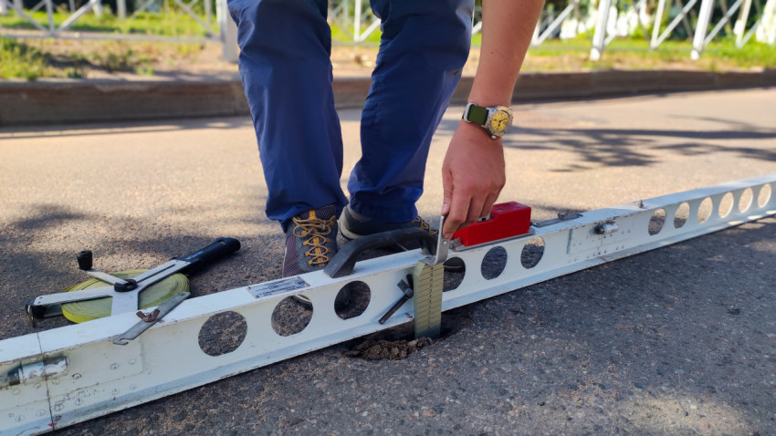 Крупно: рейка, клин-промерник и рулетка, которыми меряют неровности на асфальте