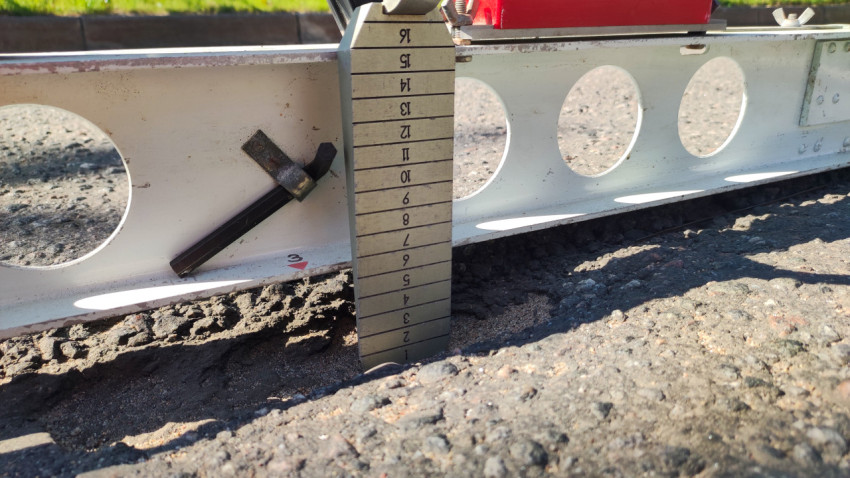 Крупный план клин-промерника под рейкой при измерении неровностей асфальта