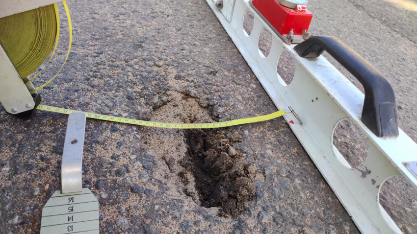 Яма в асфальте и замер рулеткой под рейкой, чтобы зафиксировать дефект покрытия