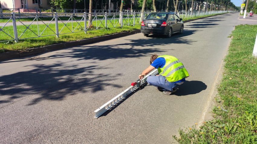 Парень в сигнальном жилете меряет ровность асфальта длинной рейкой на дороге
