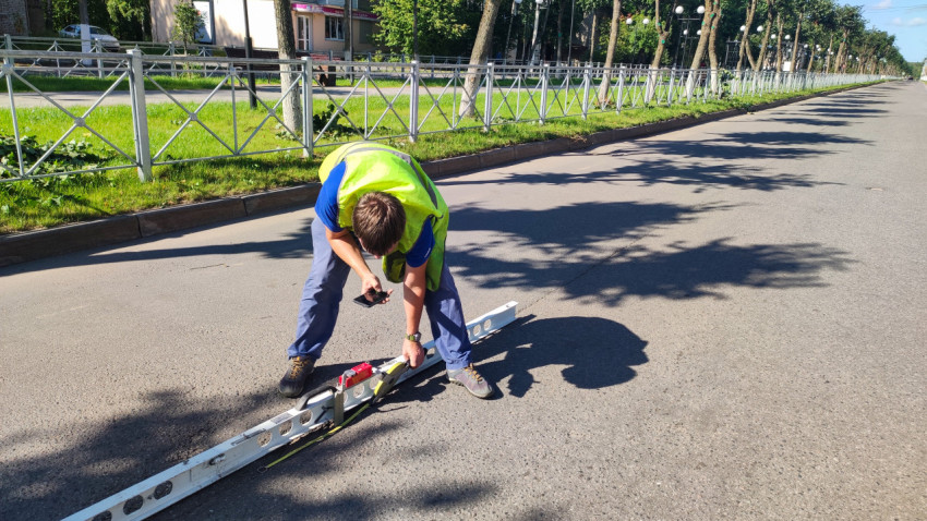 Рабочий в сигнальном жилете измеряет ровность асфальта рейкой и клин-промерником на улице