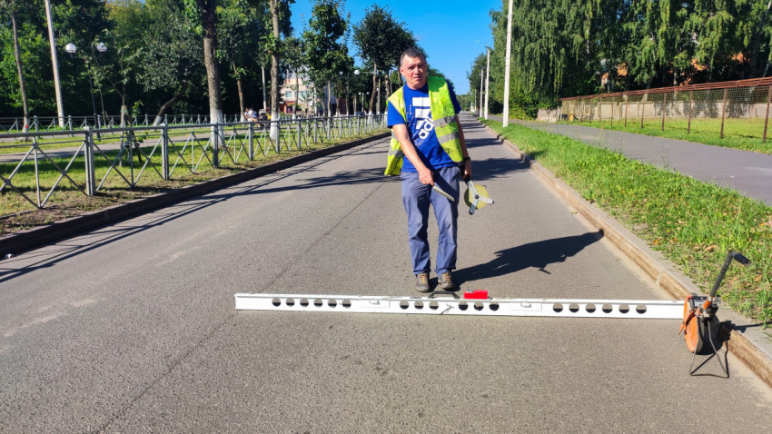 Инженер у ямы в асфальте делает замеры рулеткой и клиновым щупом рядом с мерным колесом