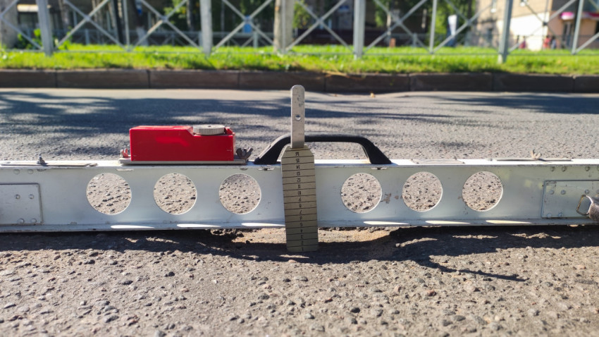 Измерительный клин под рейкой показывает величину зазора на асфальте