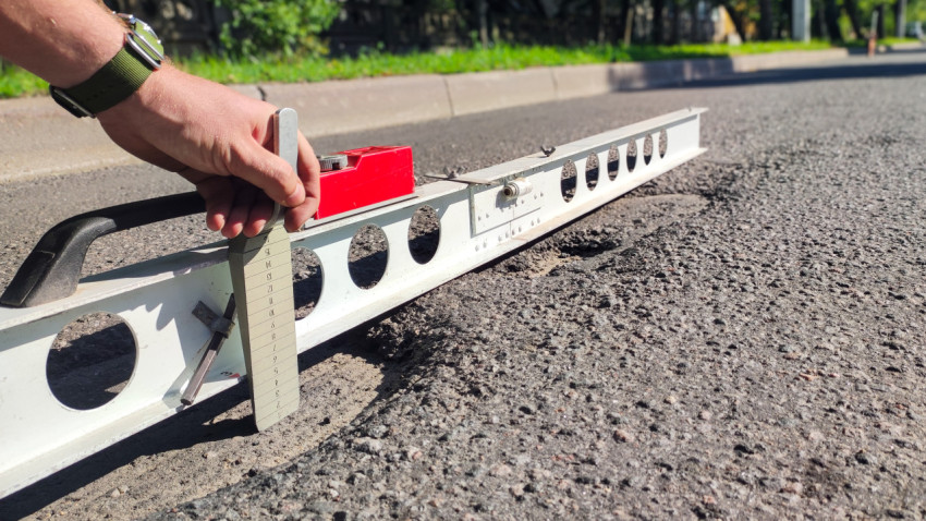 Клин-промерник под рейкой показывает просвет при замере ровности асфальта