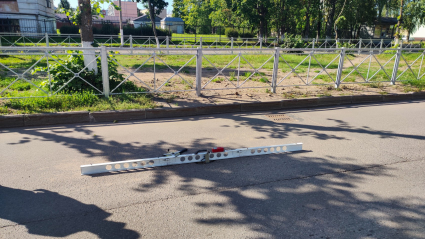 Длинная алюминиевая рейка лежит на дороге, как подготовка к замеру ровности