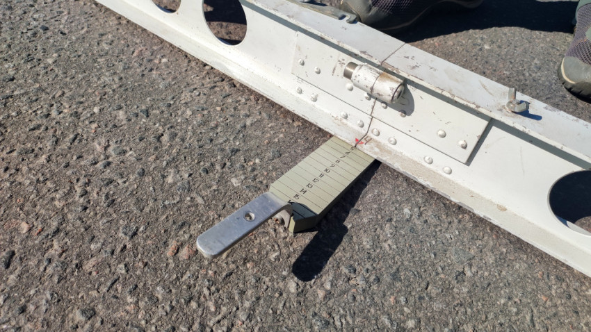 Дорожная измерительная рейка с клиновым щупом на асфальте крупным планом