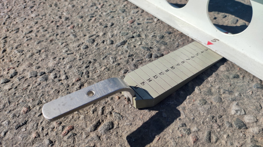 Клиновой щуп со шкалой лежит на асфальте для измерения просвета под контрольной рейкой