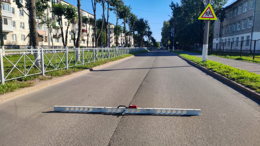 Длинная дорожная рейка лежит поперёк асфальта для проверки ровности покрытия