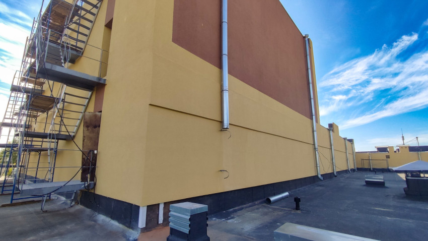 Плоская кровля с вентиляционными выходами и строительными лесами у стены крупного здания