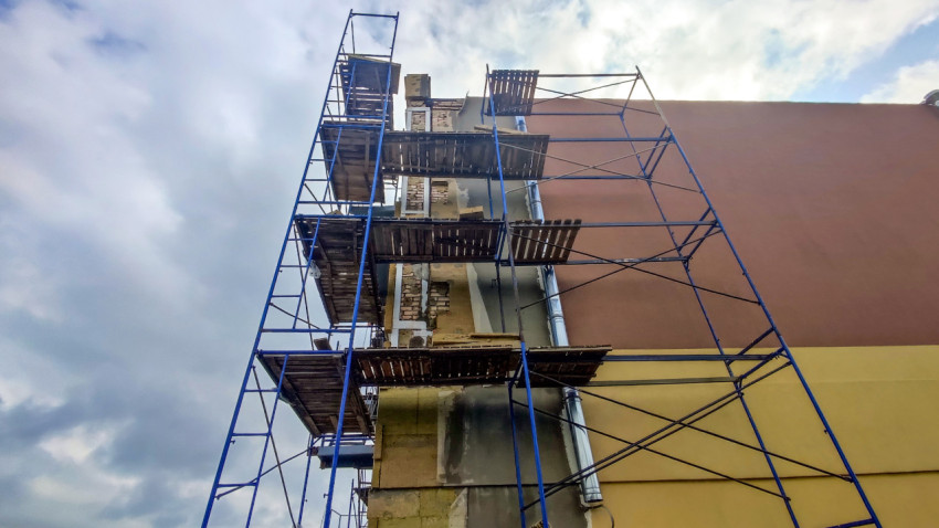 Высокие синие строительные леса у фасада с водосточной трубой и ремонтными участками