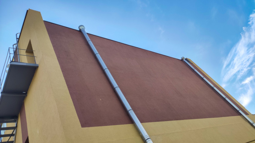 Фасад на уровне крыши с вертикальными трубами и металлической лестницей на фоне голубого неба