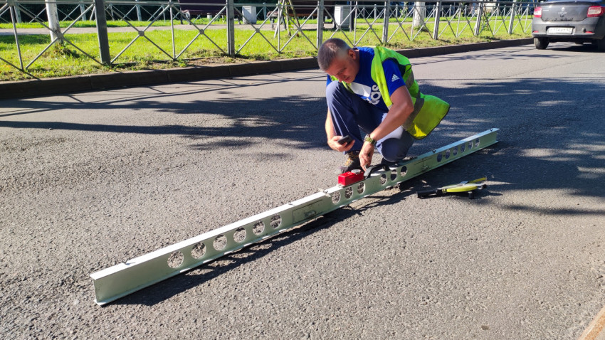 Инспектор снимает показания ровности асфальта рейкой и клином у обочины
