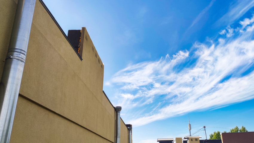 Угол фасада с парапетом и водосточной трубой на фоне неба