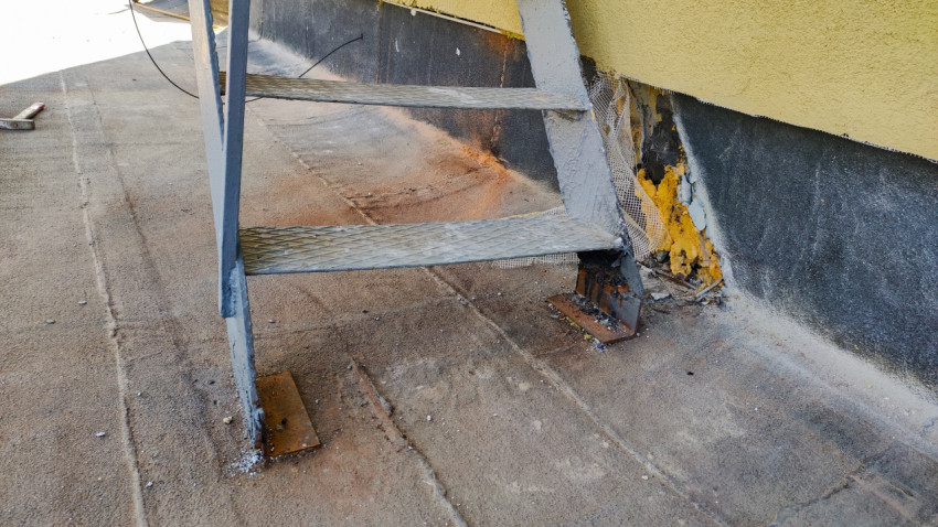 Боковой ракурс металлической лестницы у стены с повреждённой штукатуркой и утеплителем