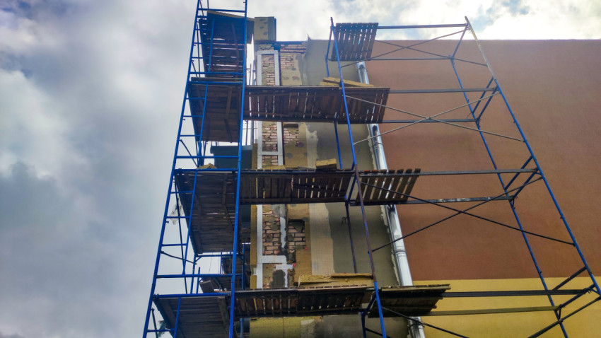 Крупный план настилов и креплений строительных лесов у ремонтируемого фасада с водостоком
