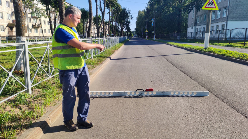 Рабочий стоит у рейки и клин-промерника, проверяя ровность асфальта