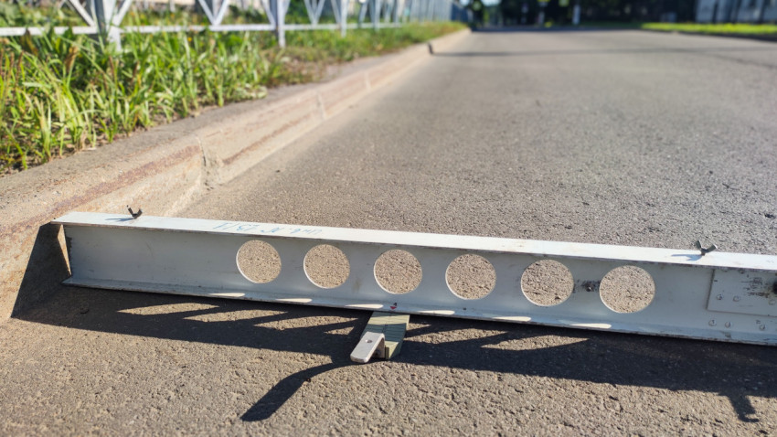 Рейка у бордюра и клин-промерник, которым проверяют просвет на асфальте