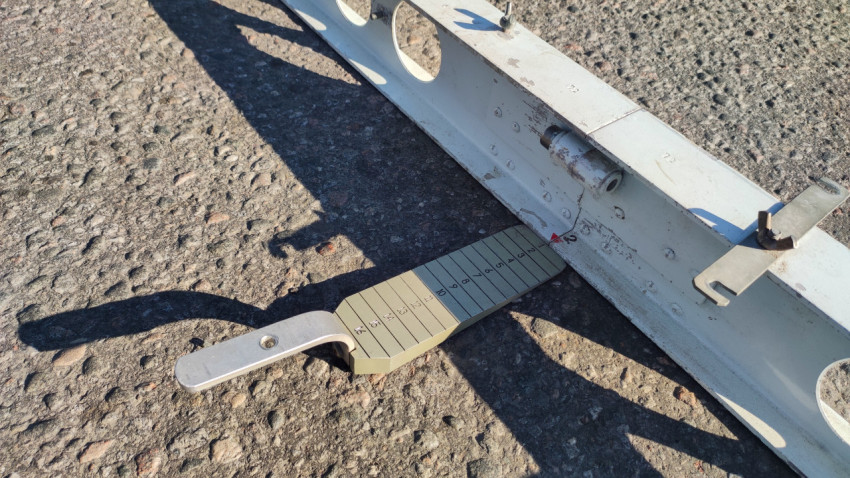 Клин-промерник под рейкой фиксирует перепад на асфальте в миллиметрах