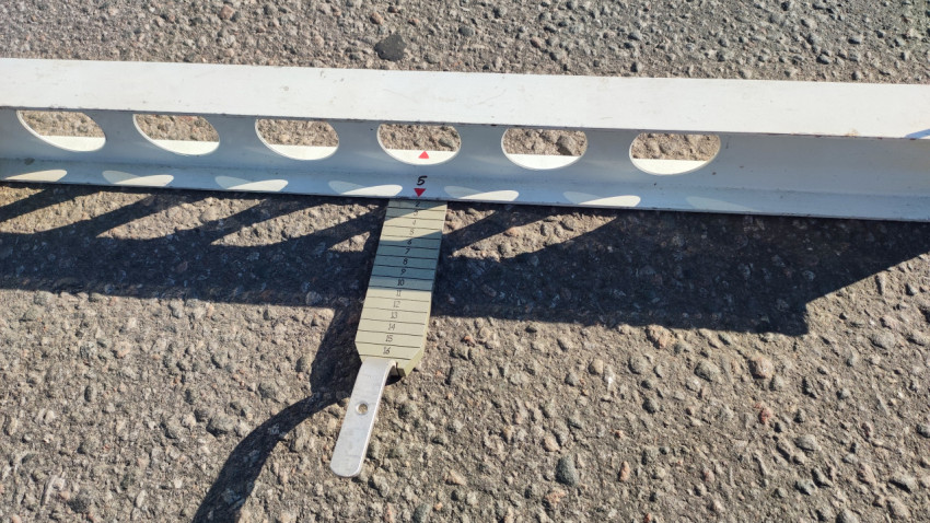 Клиновой щуп со шкалой вставлен под контрольную рейку для замера просвета на асфальте