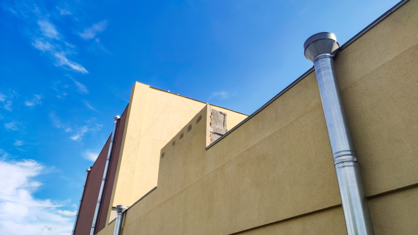 Водосточная труба и вентиляционный стояк на фасаде у кровли