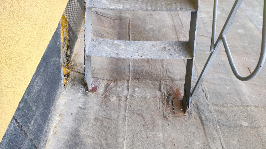 Металлическая лестница с рифлёными ступенями на плоской кровле у фасада здания