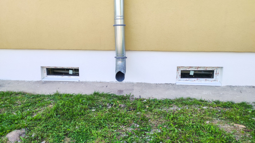 Цоколь здания с водосточной трубой и подвальными окнами на уровне травы у фасада