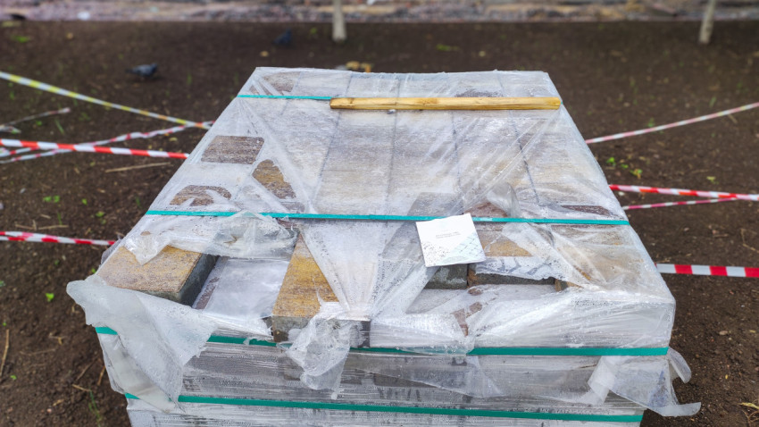 Упакованный поддон с тротуарной плиткой и бордюрами на строительной площадке