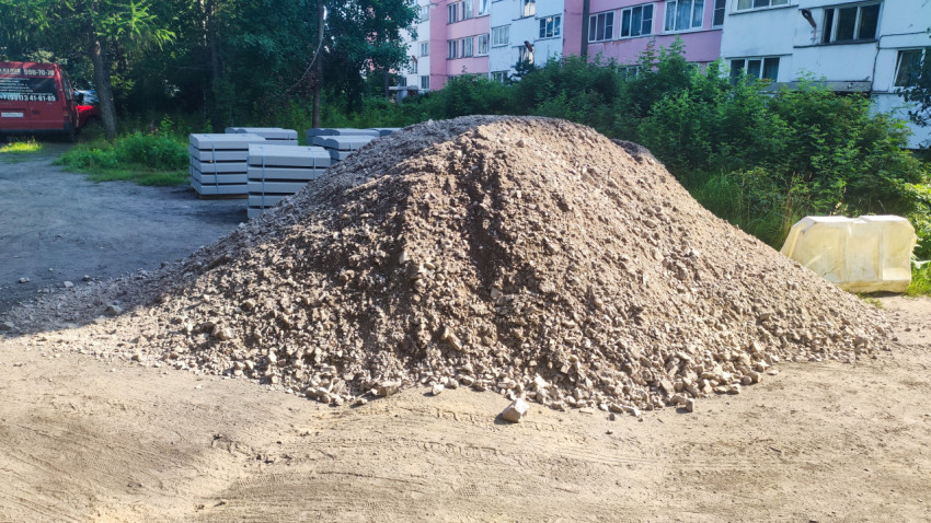 Куча щебня и стопки бетонных бордюрных камней на площадке для благоустройства двора
