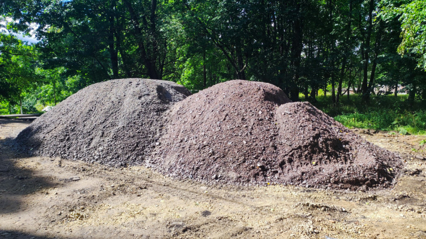 Кучи щебня и асфальтовой крошки на грунтовой площадке у лесополосы