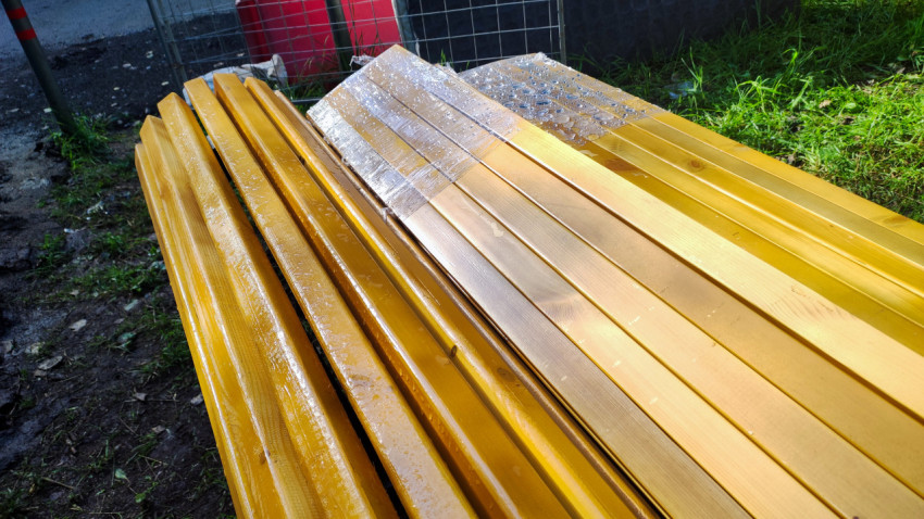 Верх скамейки с мокрыми деревянными рейками и упаковочной плёнкой после дождя