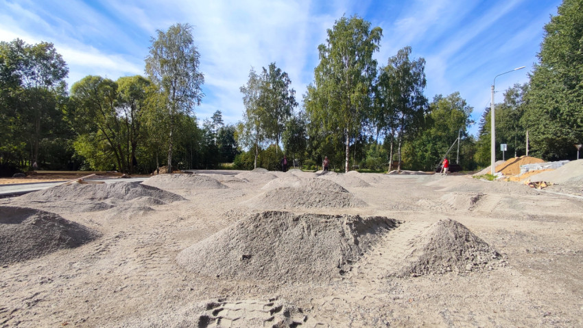 Песок и щебень на площадке дорожных работ в парковой зоне среди деревьев