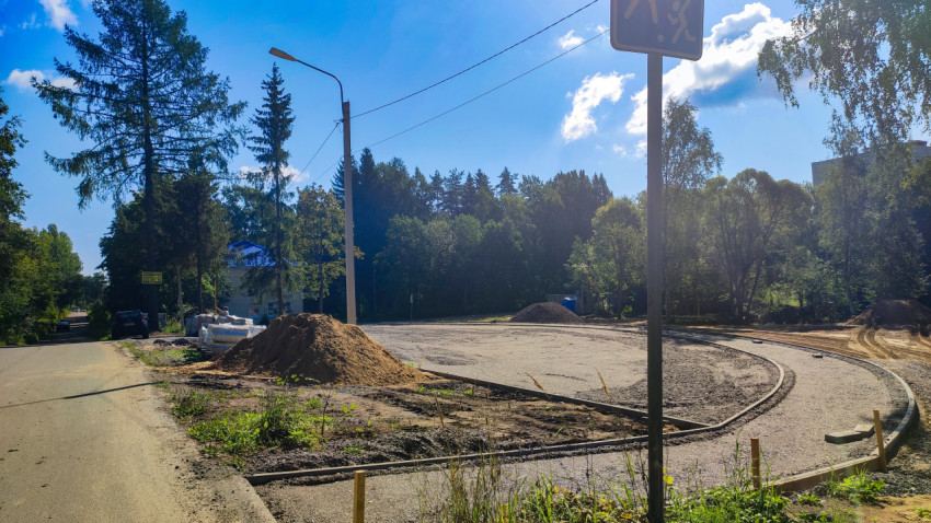 Поворот дороги с новым бордюром и кучей песка рядом с лесной полосой