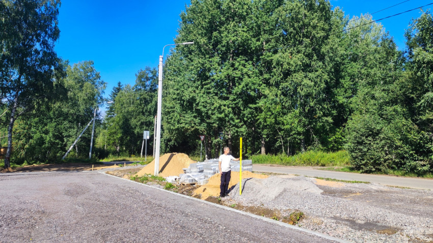 Рабочий с мерной рейкой на участке дорожных работ у перекрёстка в зелёной зоне