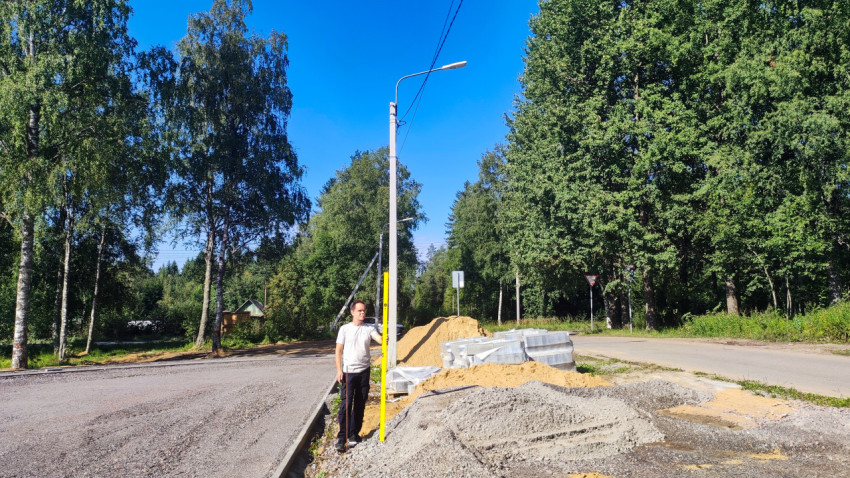 Рабочий у края дороги проверяет уровень подсыпки мерной рейкой рядом с бордюрами