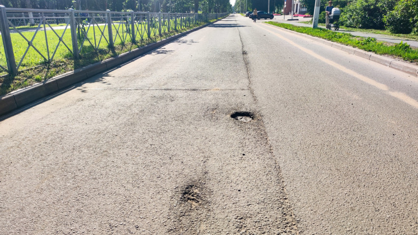 Яма на асфальтовой дороге рядом с тротуаром и пешеходным ограждением