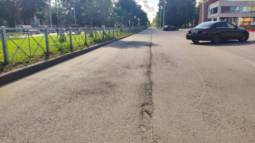 Изношенный продольный шов асфальта и автомобиль у обочины на спокойной городской улице