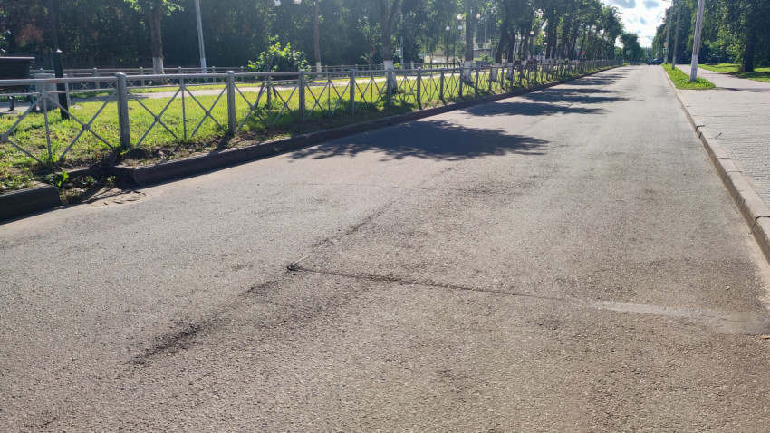 Заплатка и следы ремонта на асфальтовой дороге у бордюра и пешеходного ограждения