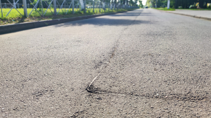 Низкий ракурс асфальтовой дороги с трещиной у бордюра и металлическим ограждением