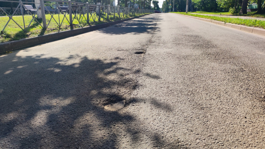 Участок асфальта с выбоинами и ямами на проезжей части у ограждения и зелёной полосы