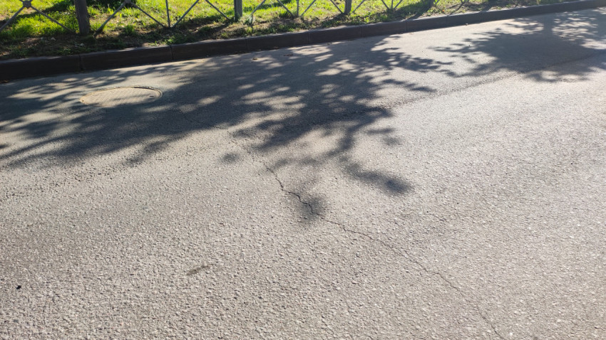 Крупный план люка колодца у бордюра на асфальте со следами износа и трещинами покрытия