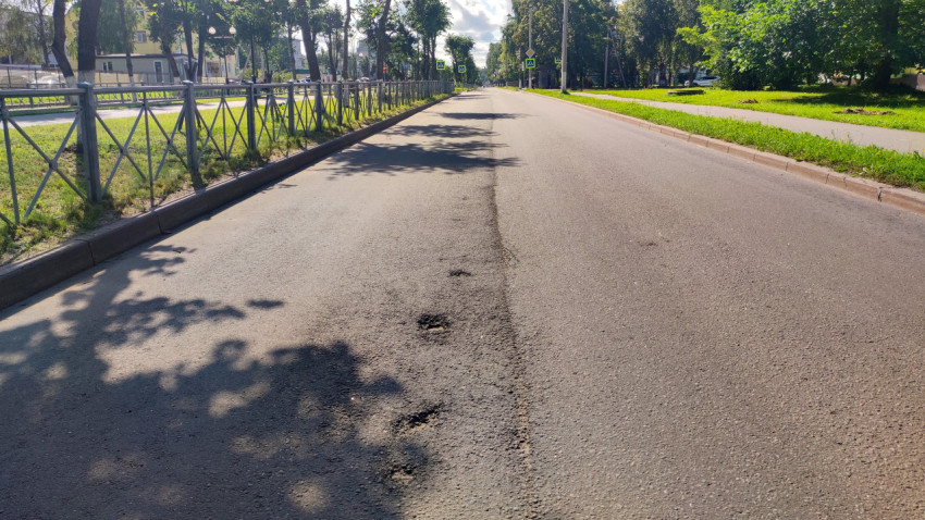 Длинная перспектива улицы с асфальтовыми заплатками, ограждением и знаками пешеходного перехода