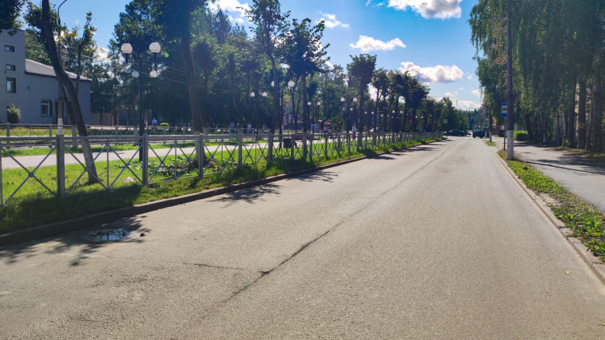 Улица в жилом районе с дорожными знаками, зелёной полосой и автобусной остановкой в перспективе